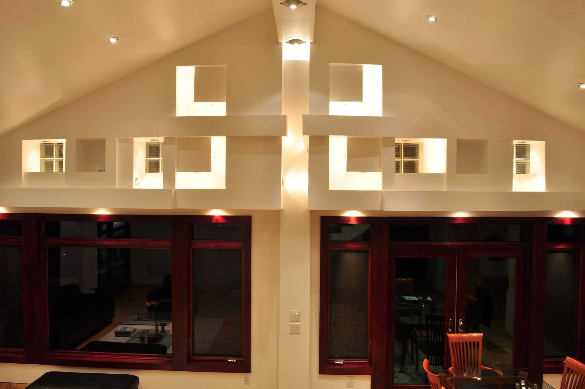 Symmetrical room with warm ceiling lights and large dark windows, viewed from inside at night