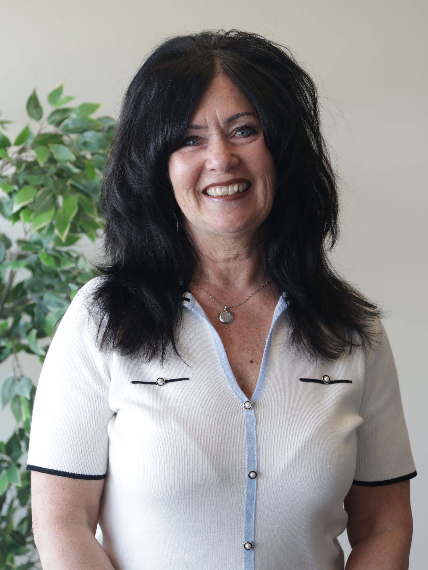 A woman with long black hair is wearing a white shirt and smiling.
