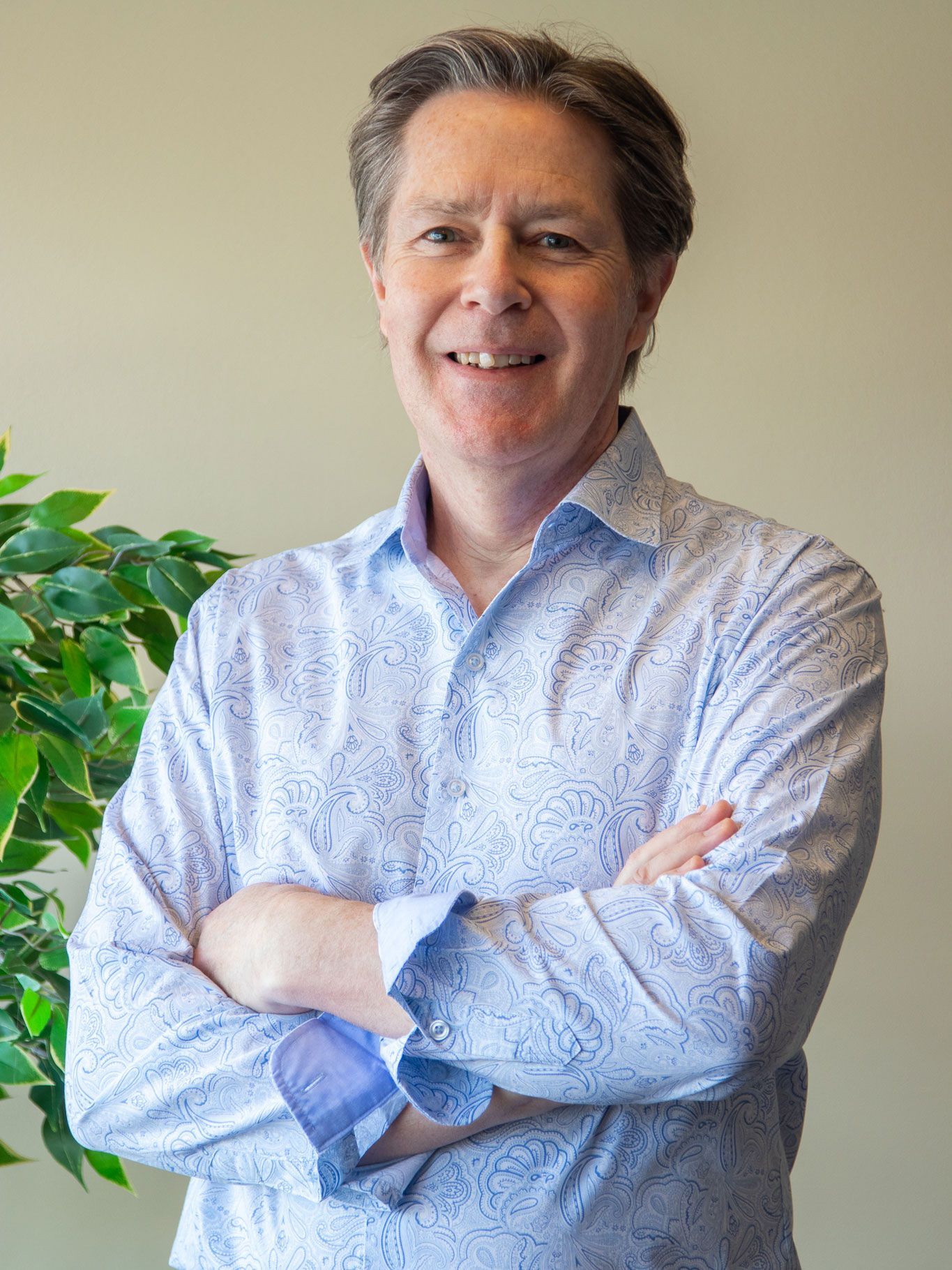 A man in a blue shirt is standing with his arms crossed and smiling.