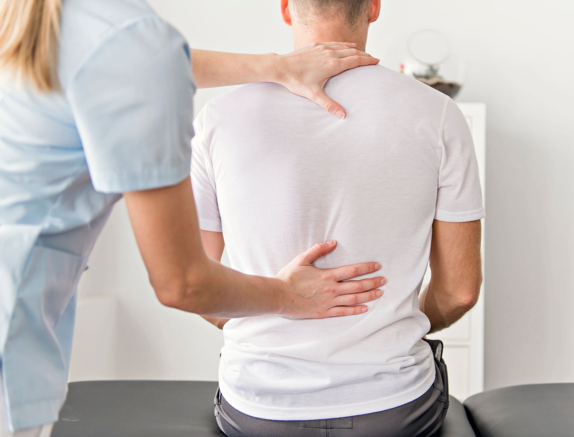 A woman is examining a man 's back while he sits on a table.