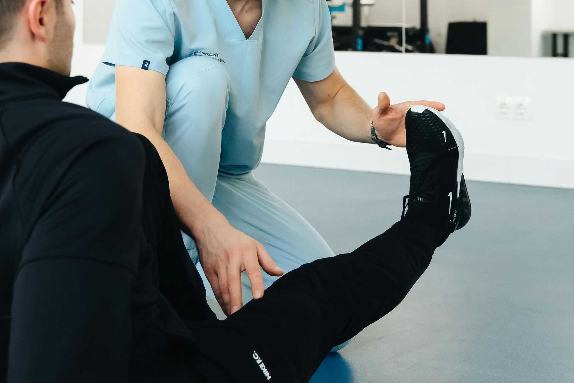 A man is stretching his leg while a nurse looks on.