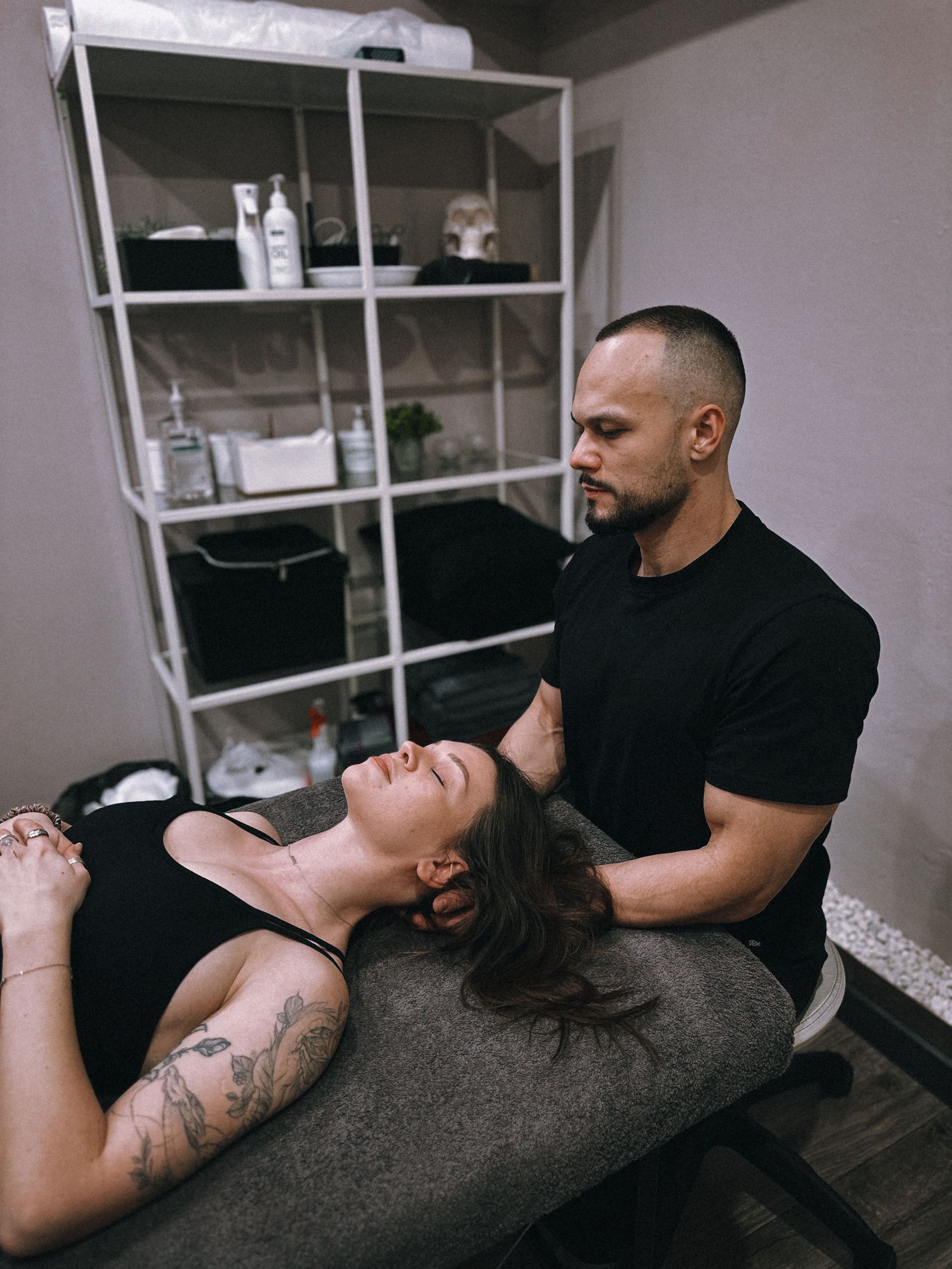 Two people in a spa room, one receiving a neck massage on a treatment table.
