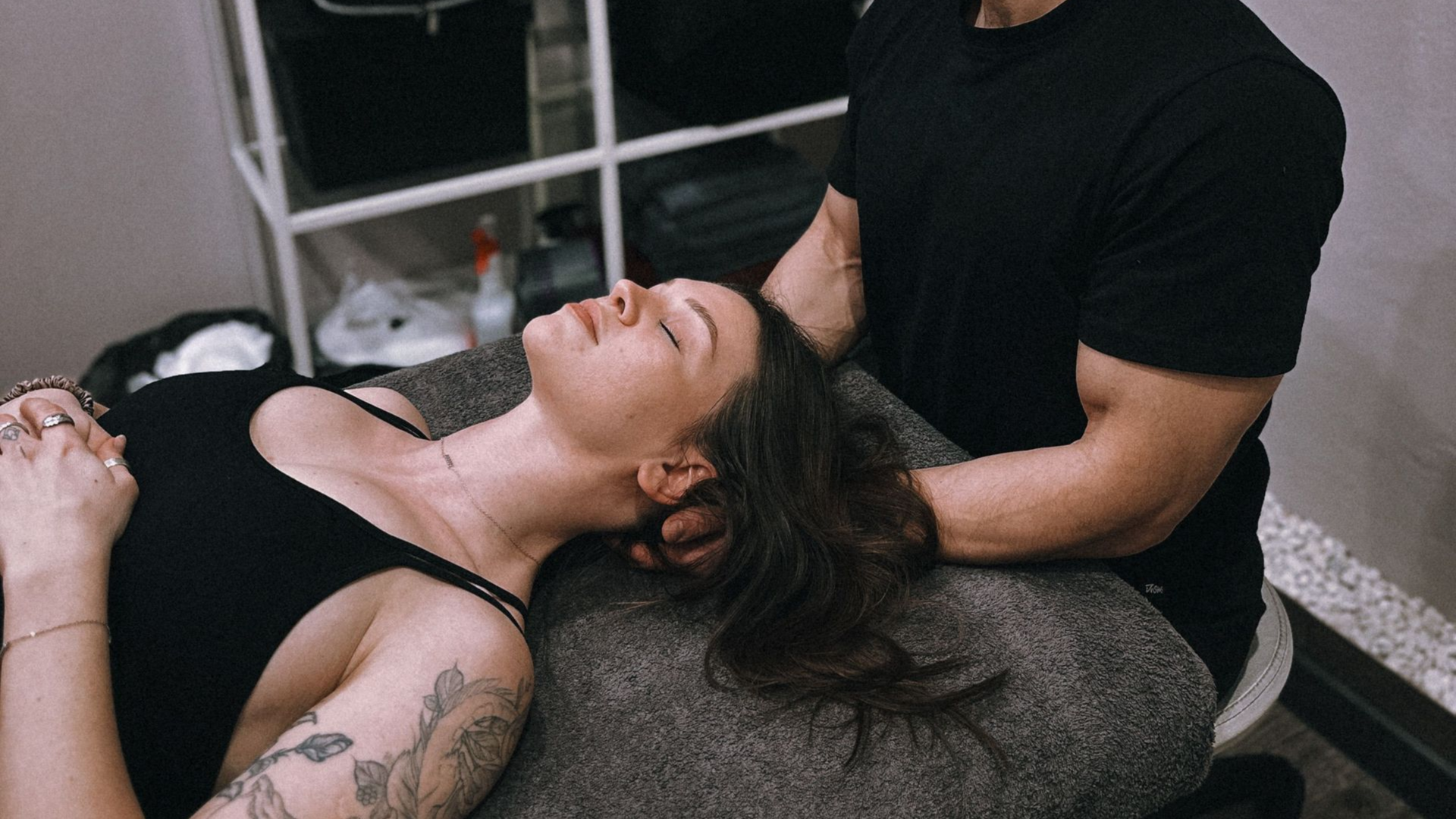 Person receiving a shoulder massage while lying on a table in a salon.
