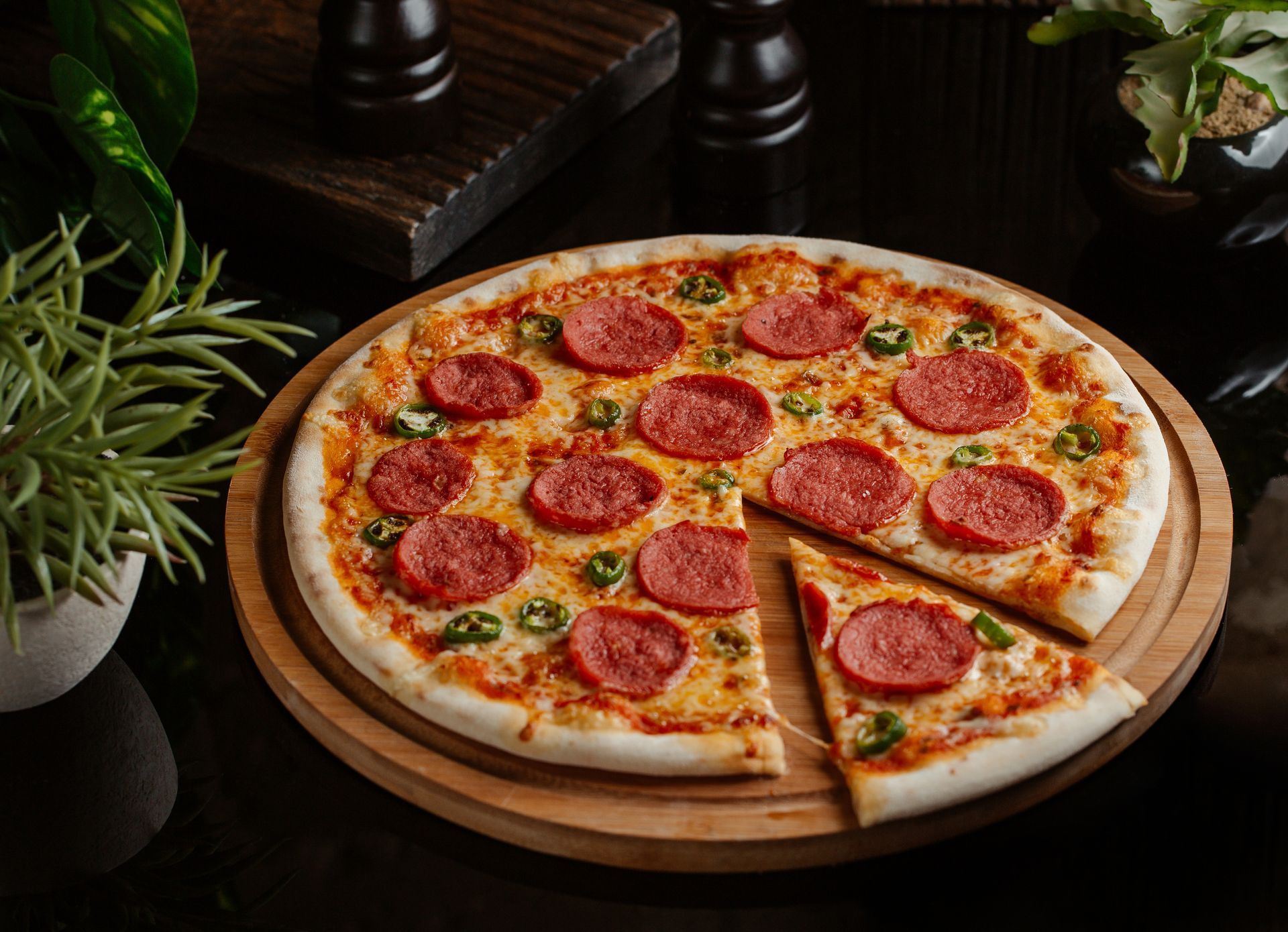 A pepperoni pizza on a wooden cutting board with a slice taken out of it.