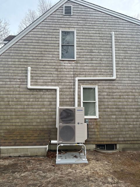 A gray brick house with a white pipe coming out of the side of it.