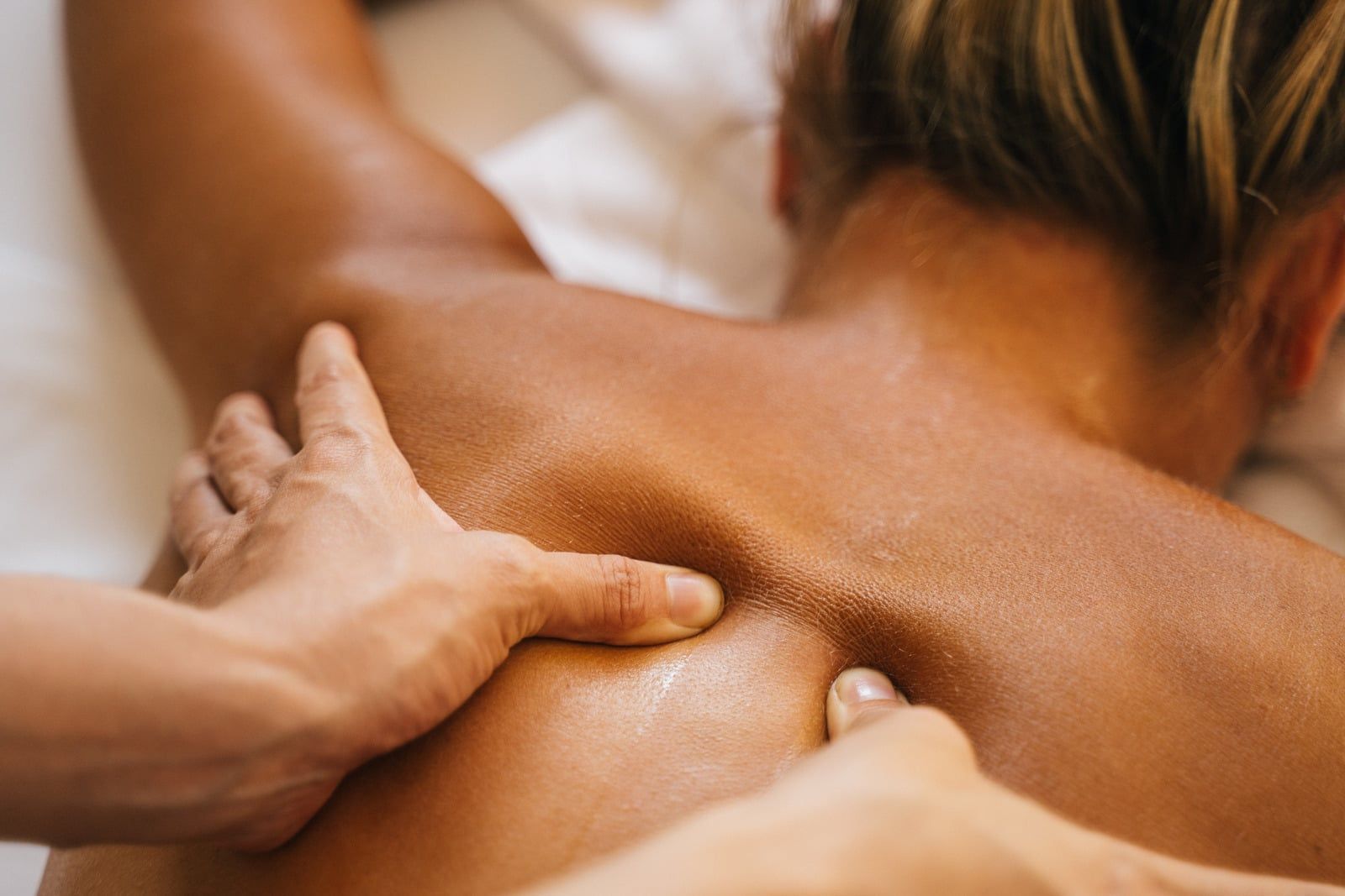 Hands massaging a person’s bare back and shoulder in a spa setting