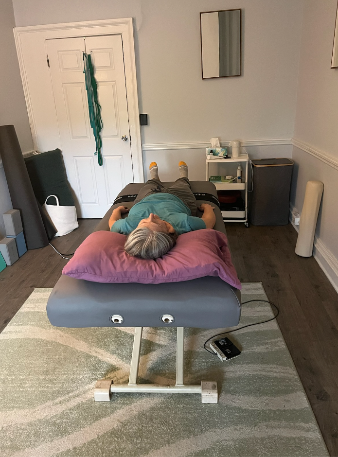 Person lying face down on a massage table in a small treatment room.