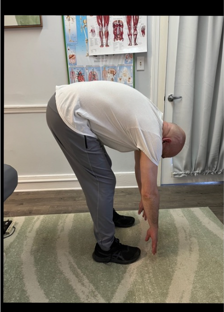 Person bending forward in a clinic, touching the floor during a flexibility assessment