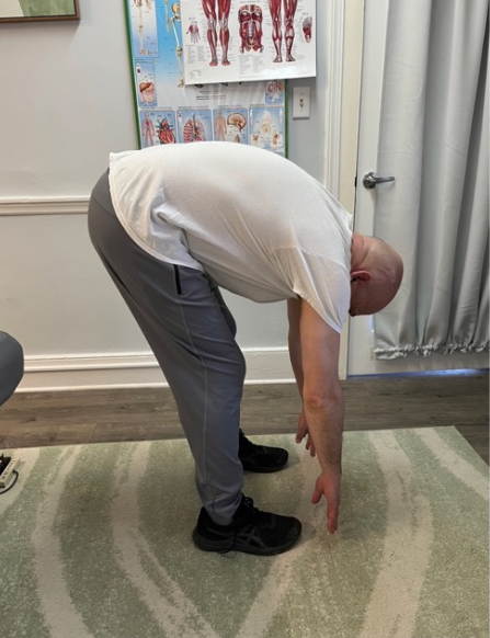 Person in a clinic bending forward to touch toes during a back stretch test.