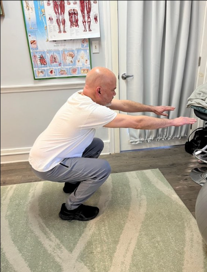 Person doing a squat exercise indoors on a rug, reaching arms forward toward a pink pad.