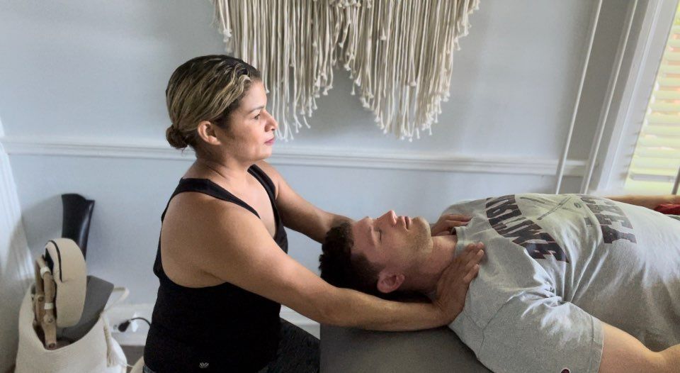 Therapist performing a neck massage on a man lying on a treatment table in a bright room