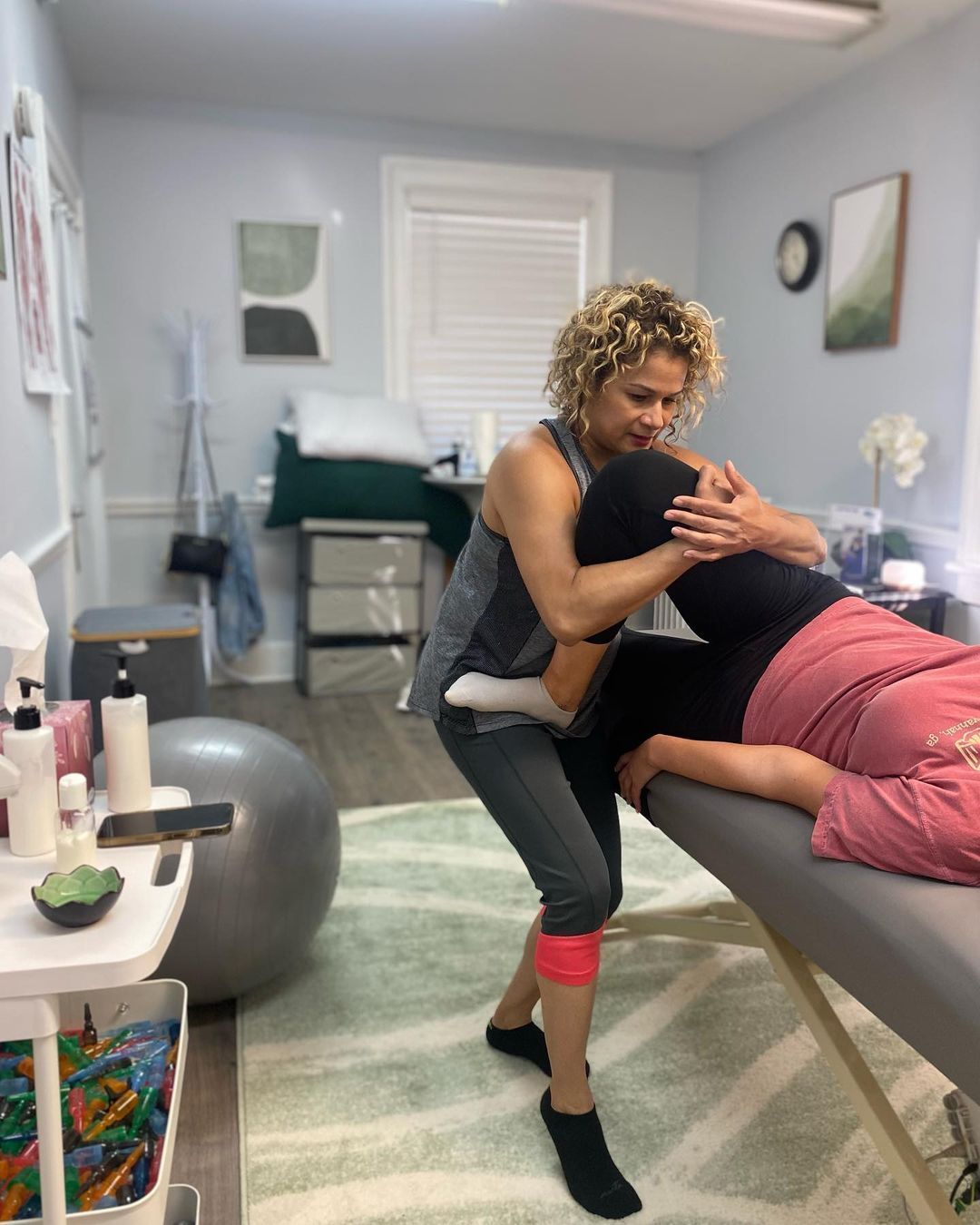 Physical therapist assisting a patient on a treatment table in a bright clinic room