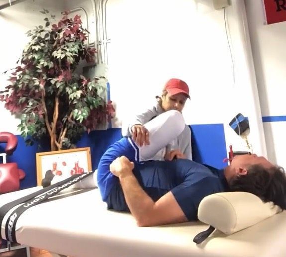 Physical therapy session: therapist in red cap stretching a man lying on a treatment table.