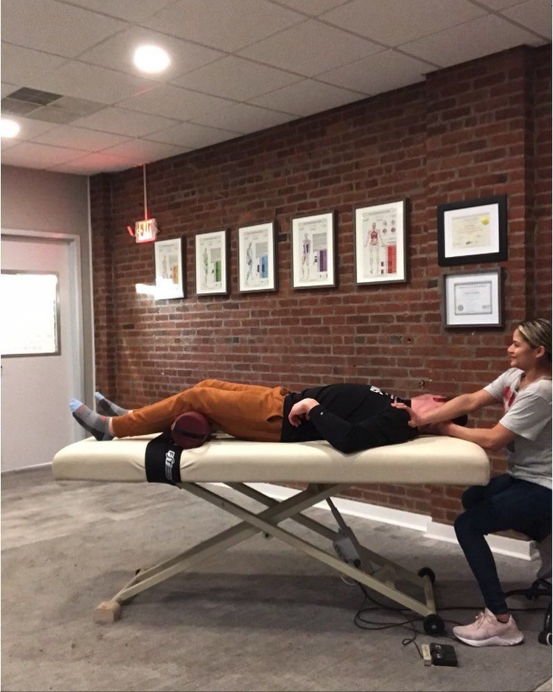 Person lying on a massage table while another person massages their legs in a clinic room.