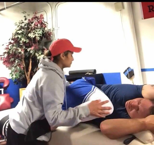 Person in red cap assists another person lying on a mat during a stretching or therapy session.