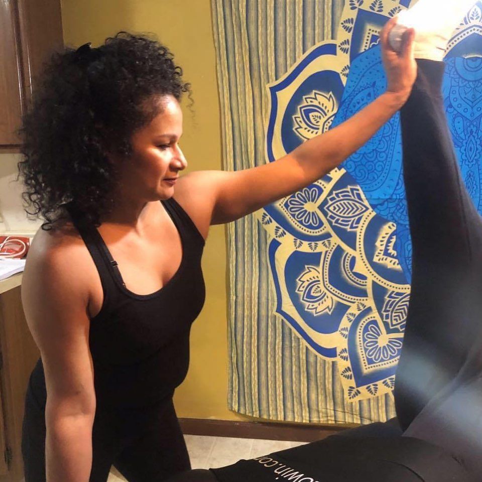 Woman in a black tank top stretching with one arm raised beside a blue mandala wall hanging