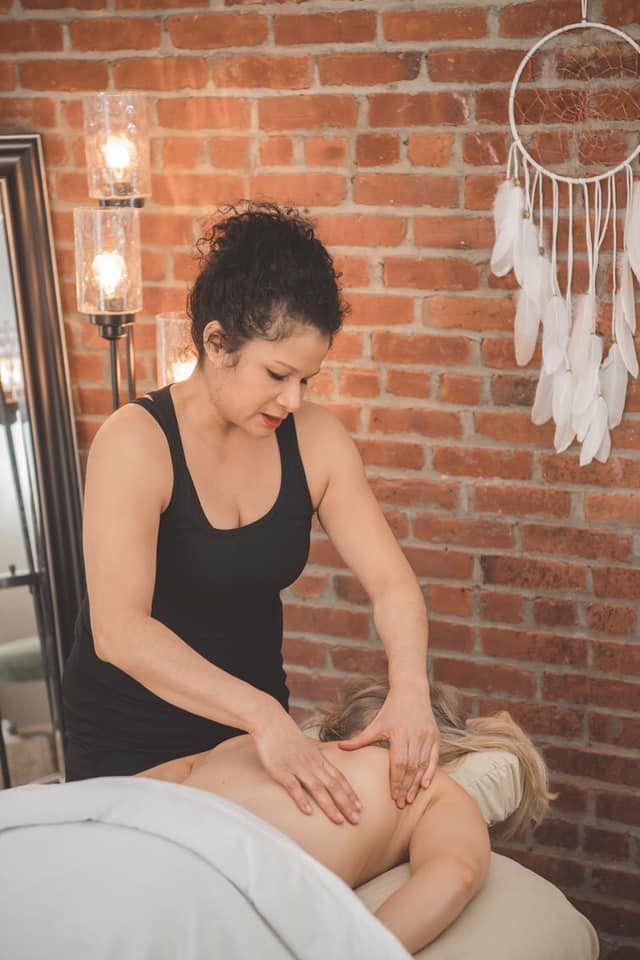 Massage therapist working on a client’s back in a brick-walled spa room with a dreamcatcher.