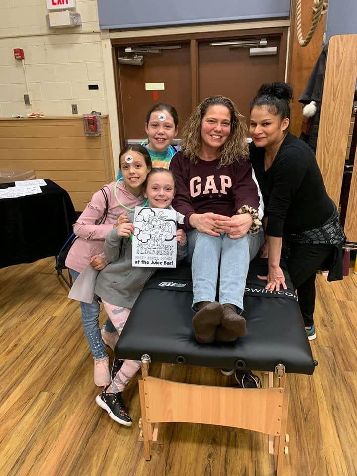 Five people posing on a gym mat in a school gym, one holding a drawing, all smiling.