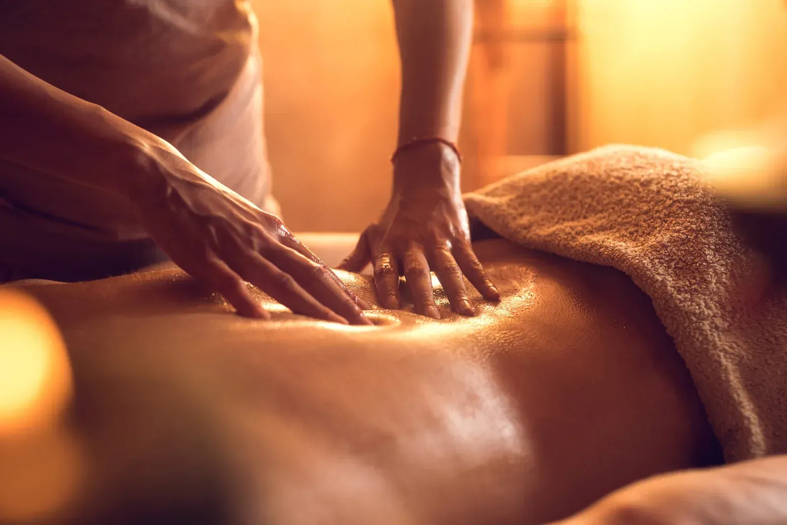Hands giving a back massage with warm oil and a towel in a spa setting