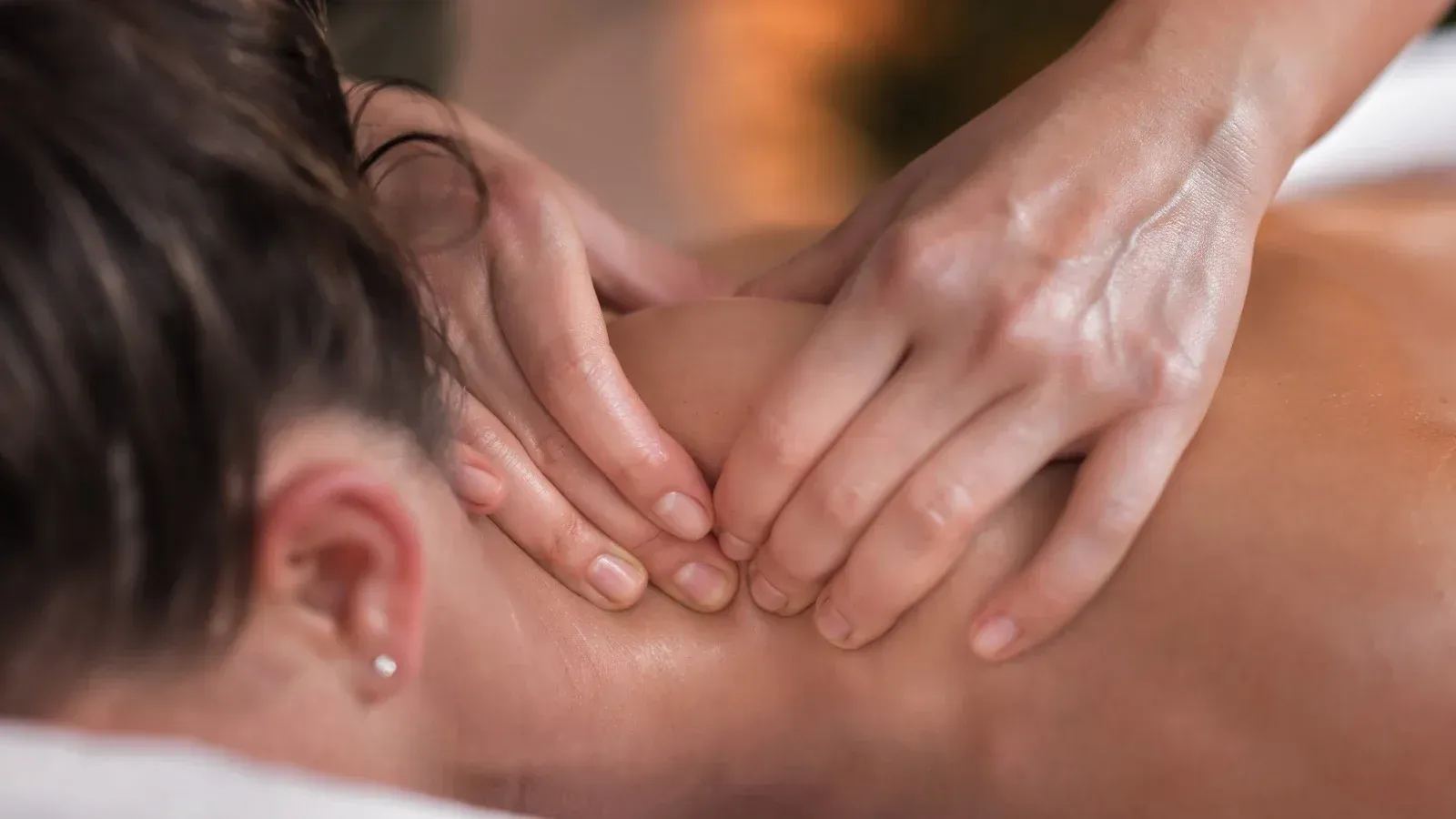 Hands massaging a person's neck and shoulder in a spa setting