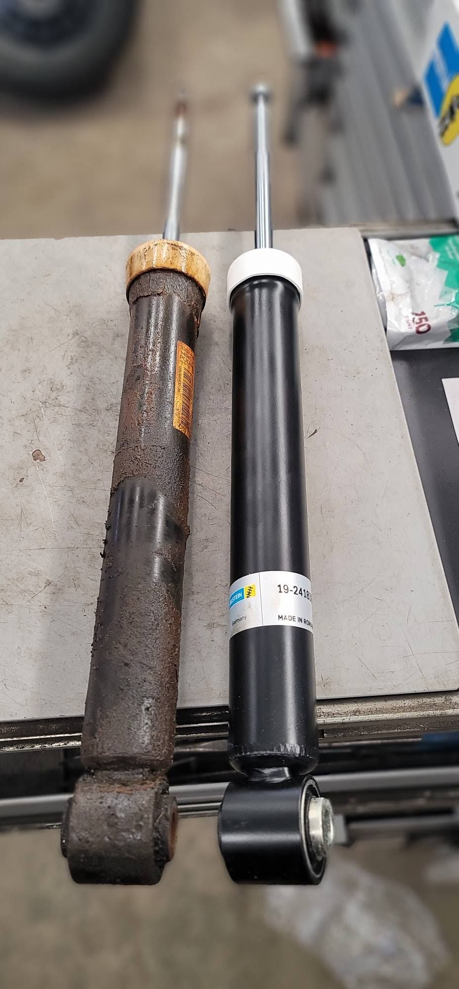 Two shock absorbers side by side on a workbench, one rusted and one black with a white bushing. | FINE Automotive Services