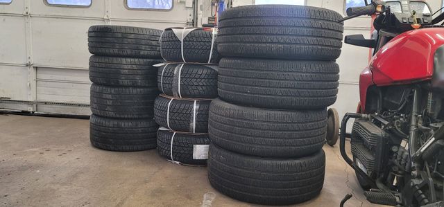 Stacks of black tires tied with white straps in a workshop, with part of a red motorcycle visible on the right. | FINE Automotive Services