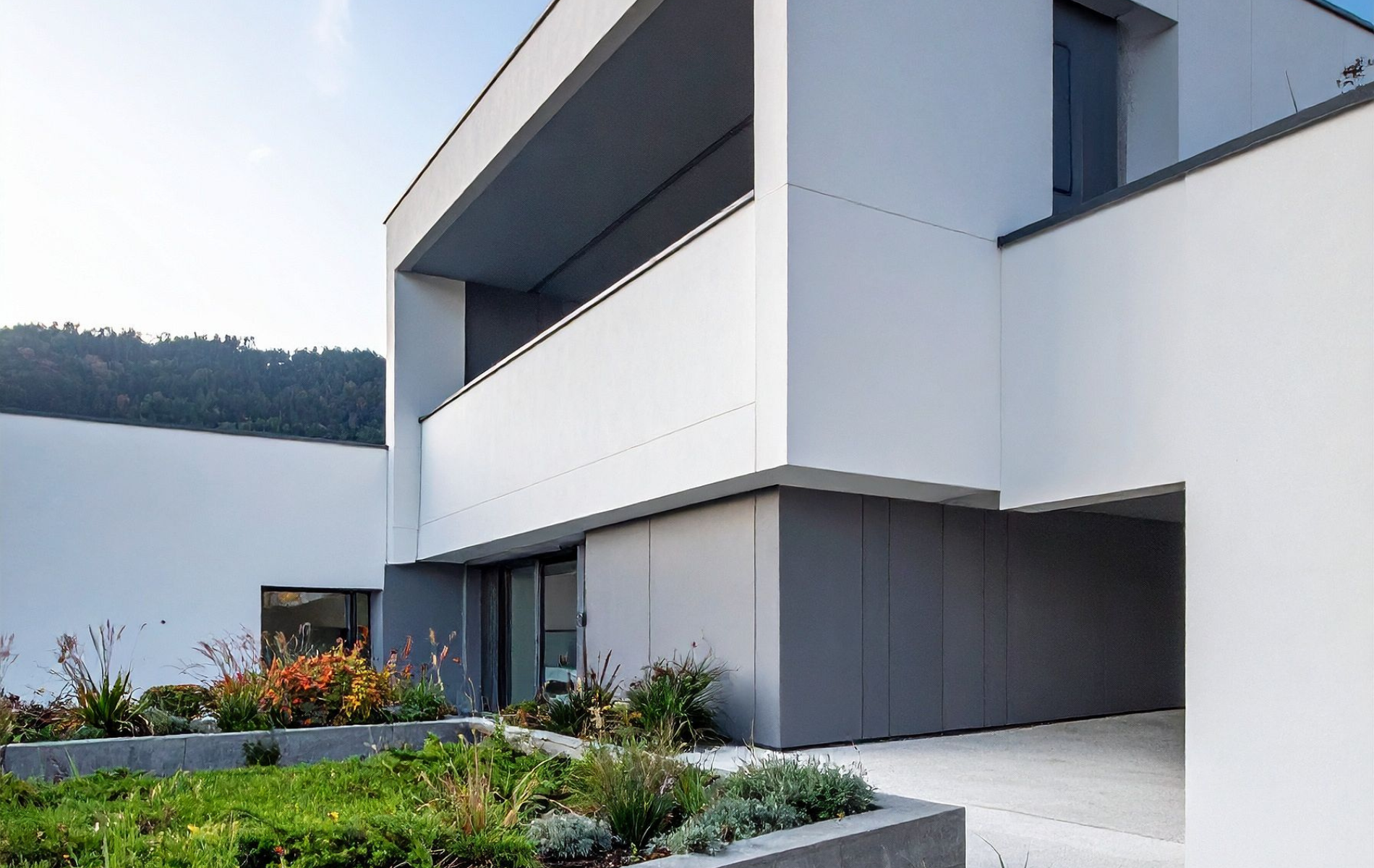 Modern white house with a balcony overlooking a lake. Gray accents, green landscaping, clear sky.