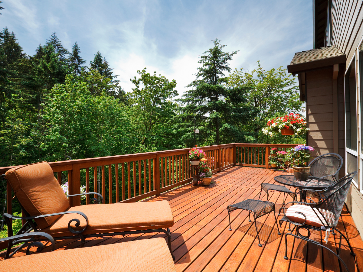Wooden deck with seating overlooking a lush green forest under a partly cloudy sky.