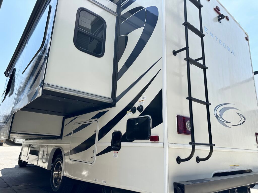 A white rv with a ladder attached to the side is parked in a parking lot.