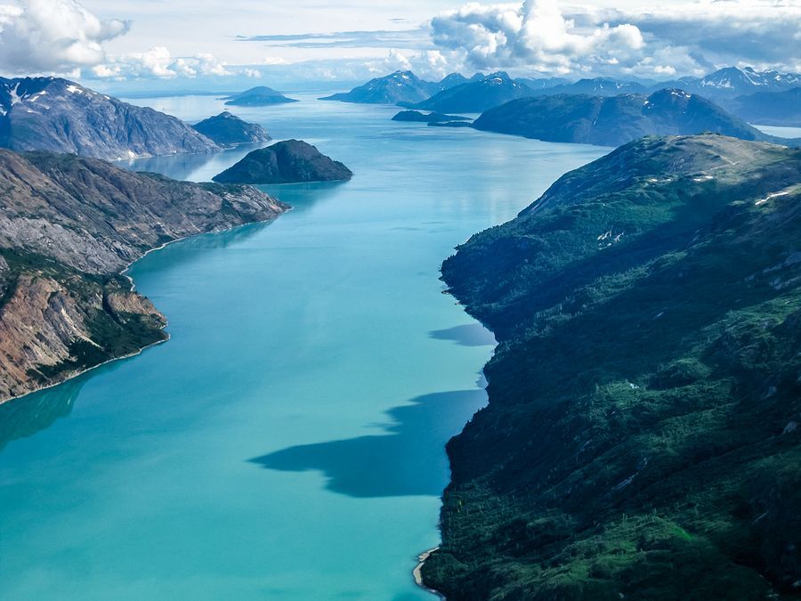 Aerial view of a turquoise fjord between dark green mountains and snow-capped peaks