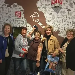 Five people smiling in front of a patterned wall with the word “Roma” and a shop logo.