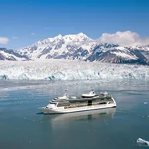 Cruise ship sailing past icy glacier and snow-covered mountains under a clear blue sky