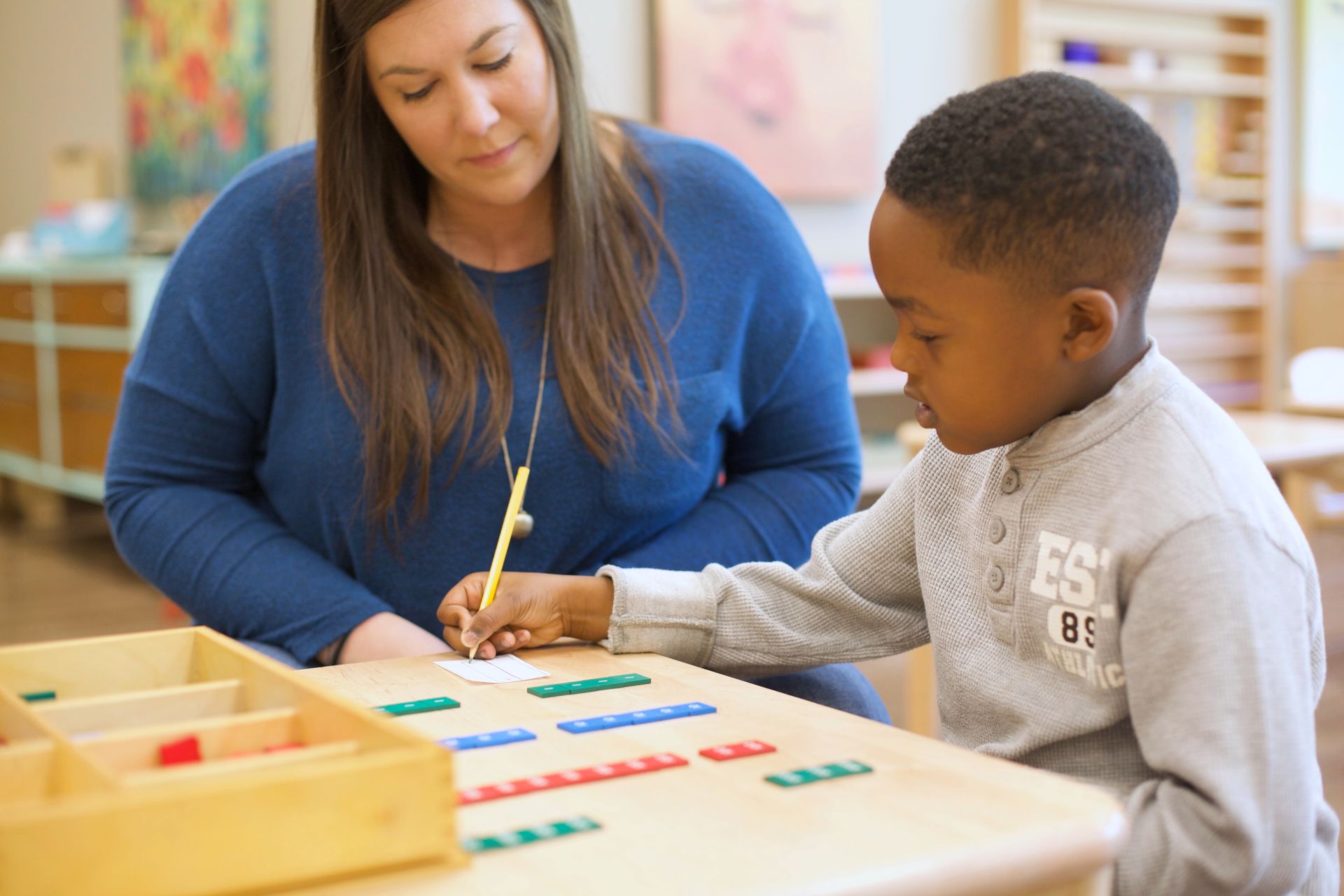 Teacher helping child with colorful counting blocks at a classroom table