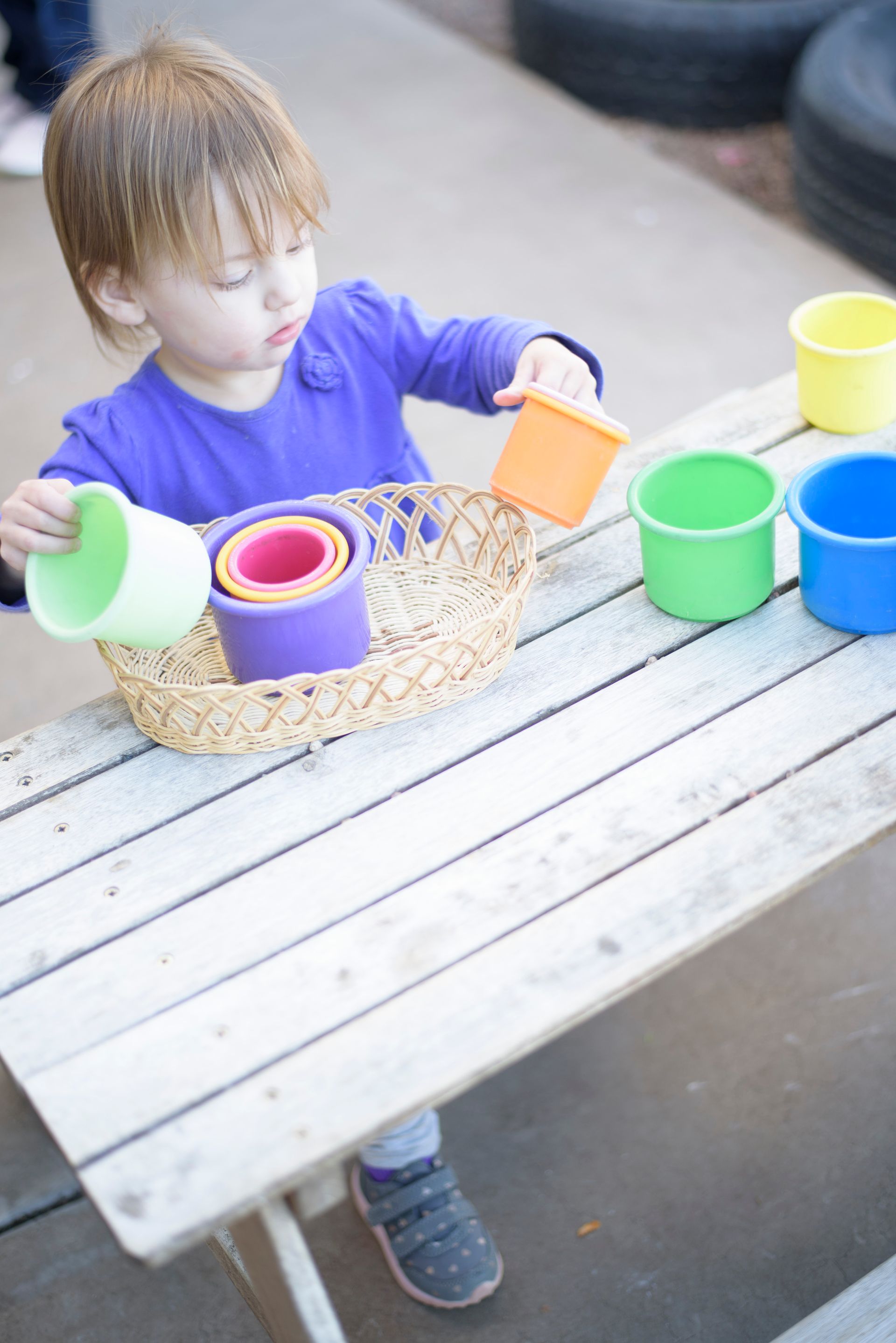 Child arranging colorful cups in a basket on a picnic table outdoors