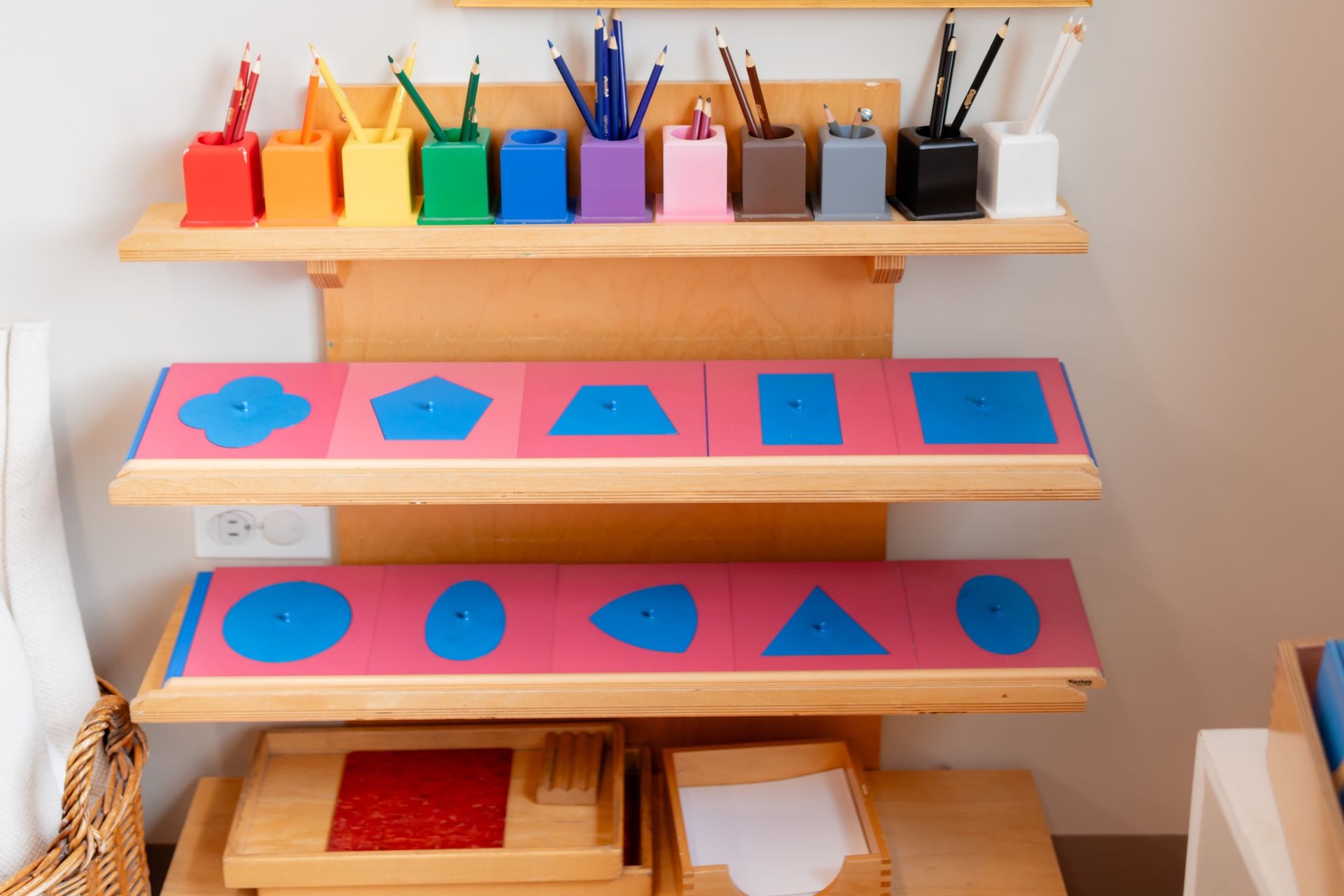 Colorful wooden shape-sorting shelves with blue geometric pieces and art supplies in the background