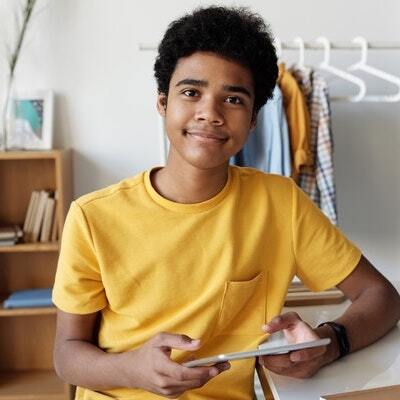 a Montessori child in a yellow shirt is sitting at a desk holding a tablet