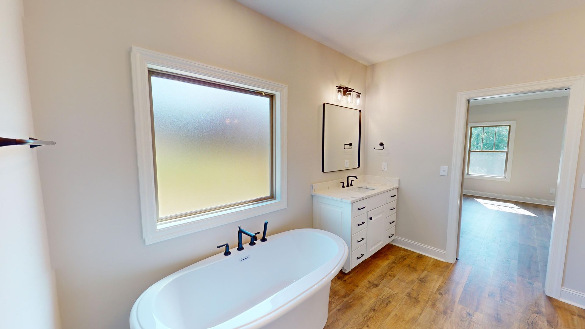 Bathroom with a white freestanding tub, vanity, frosted window, and hardwood floors.
