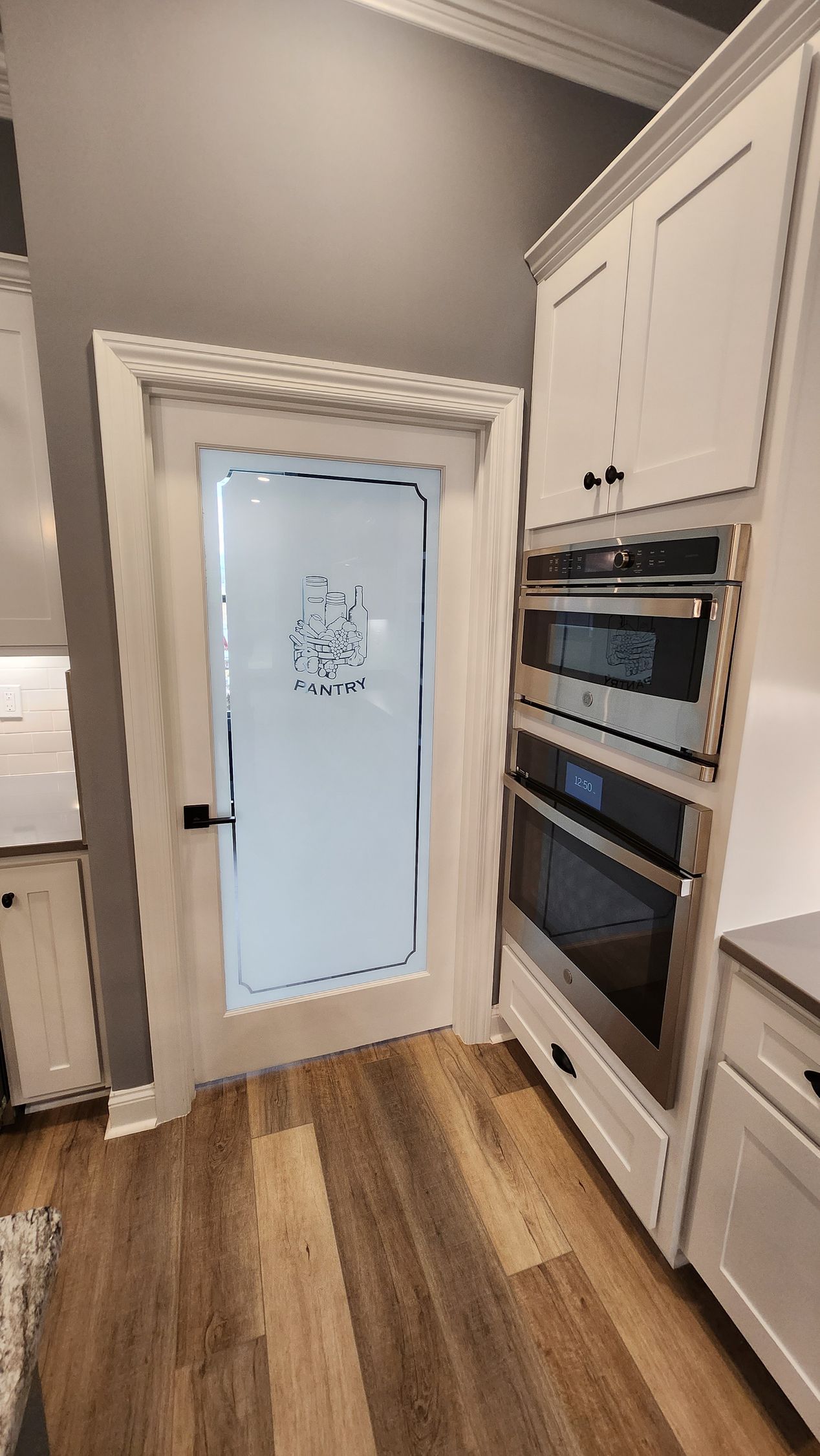 White pantry door with frosted glass, built-in ovens, and white cabinets in a kitchen.