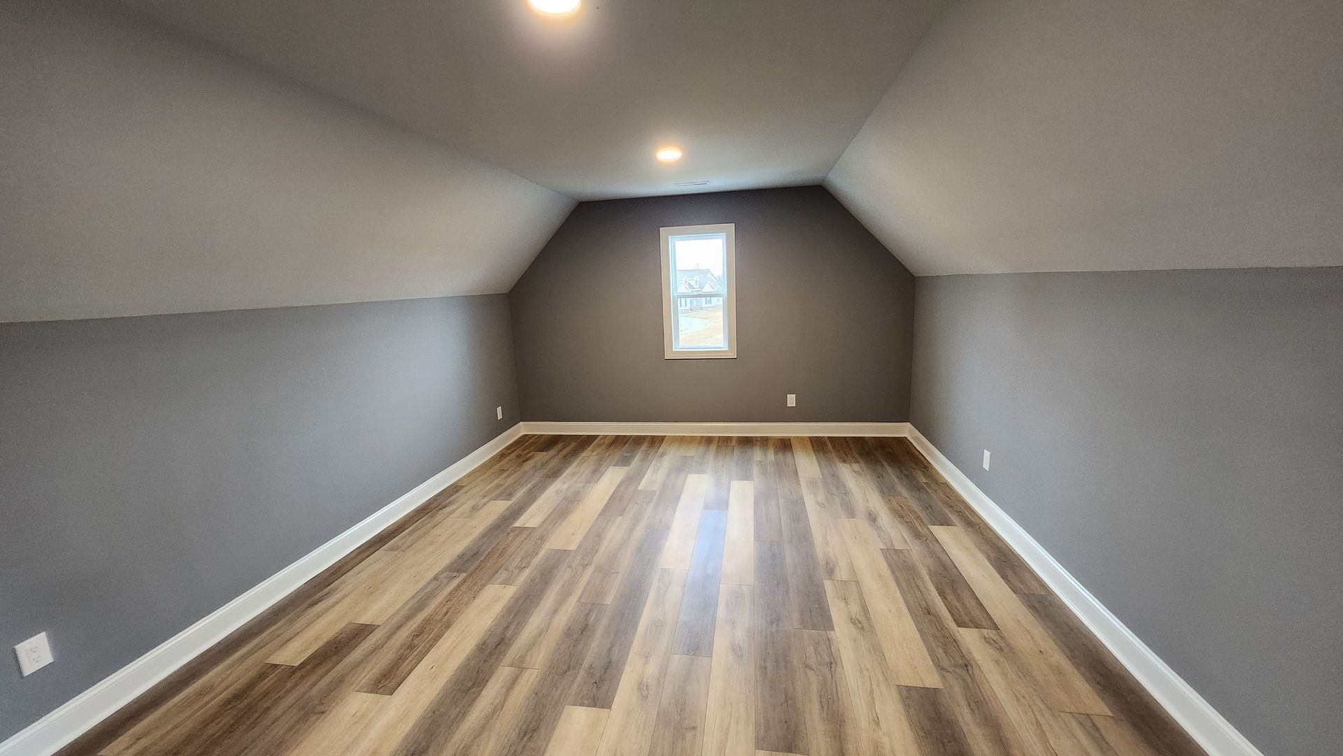 Empty attic room with gray walls, wood-look floor, and small window.