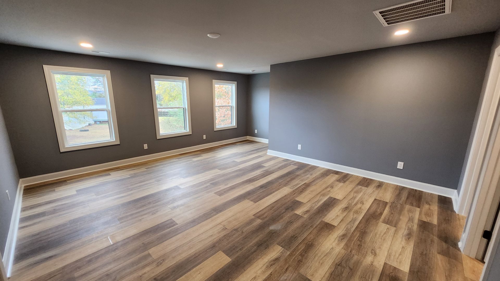 Empty room with gray walls, three windows, and wood-look flooring.