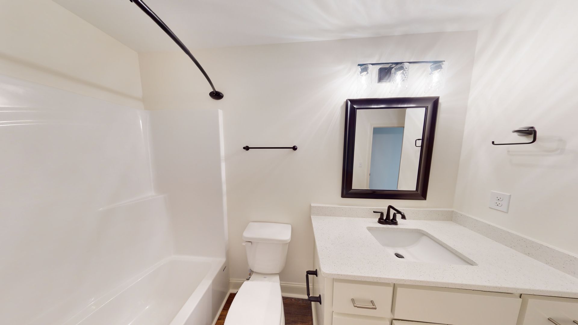 Bathroom with white bathtub, toilet, vanity, and black accents.