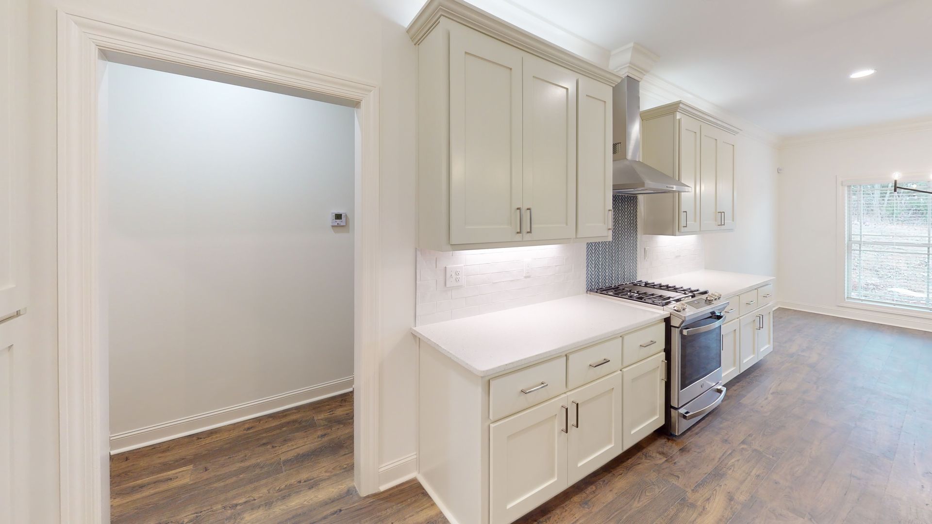 Kitchen with white cabinets, stovetop, and pantry entrance.  Light wood floor.