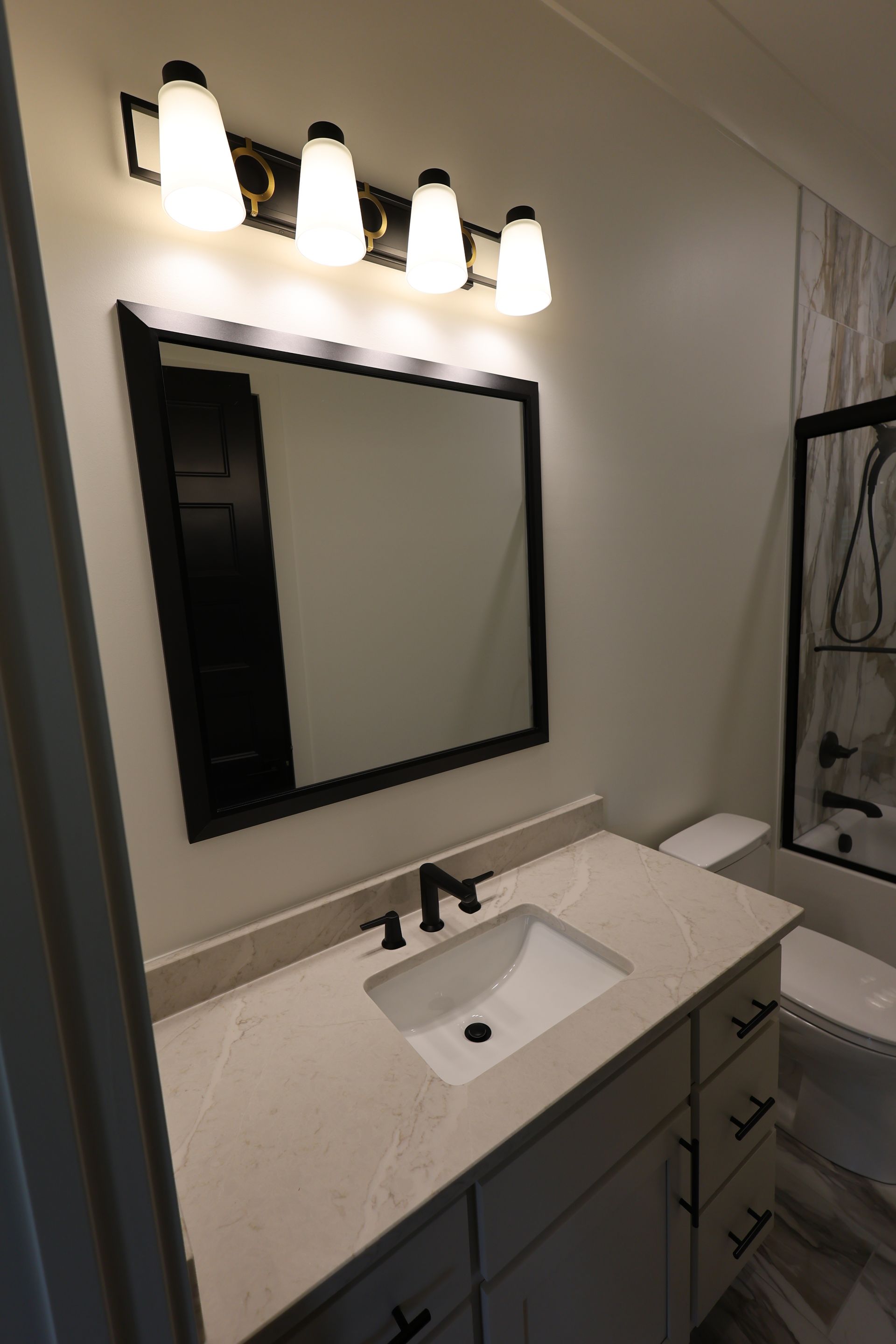 Bathroom with a vanity, mirror, and light fixture. Black fixtures and trim. Beige countertop and light walls.