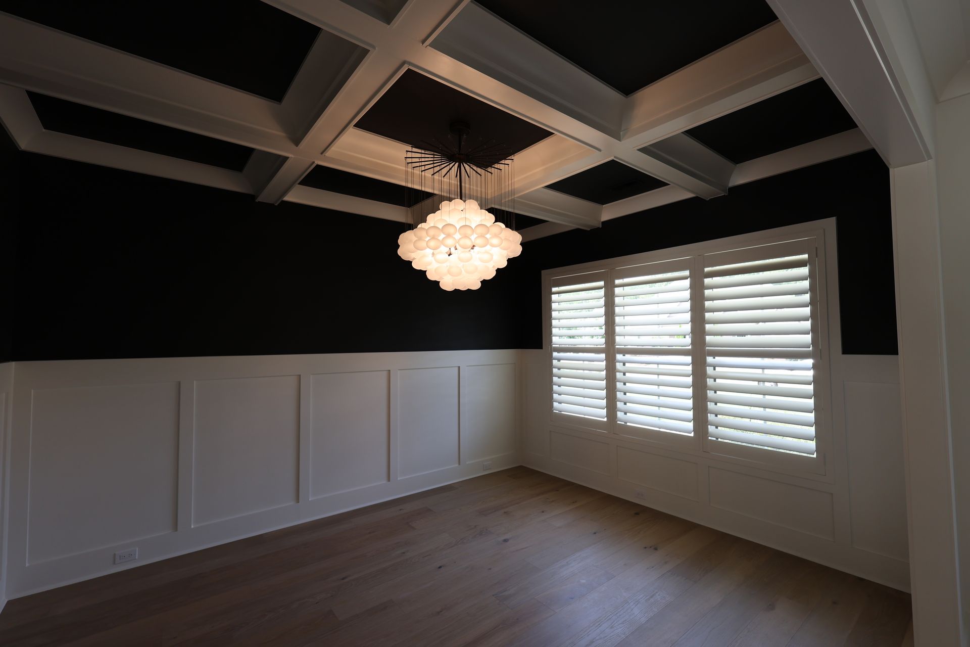 Dining room with black walls, white trim, wood floor, and chandelier.