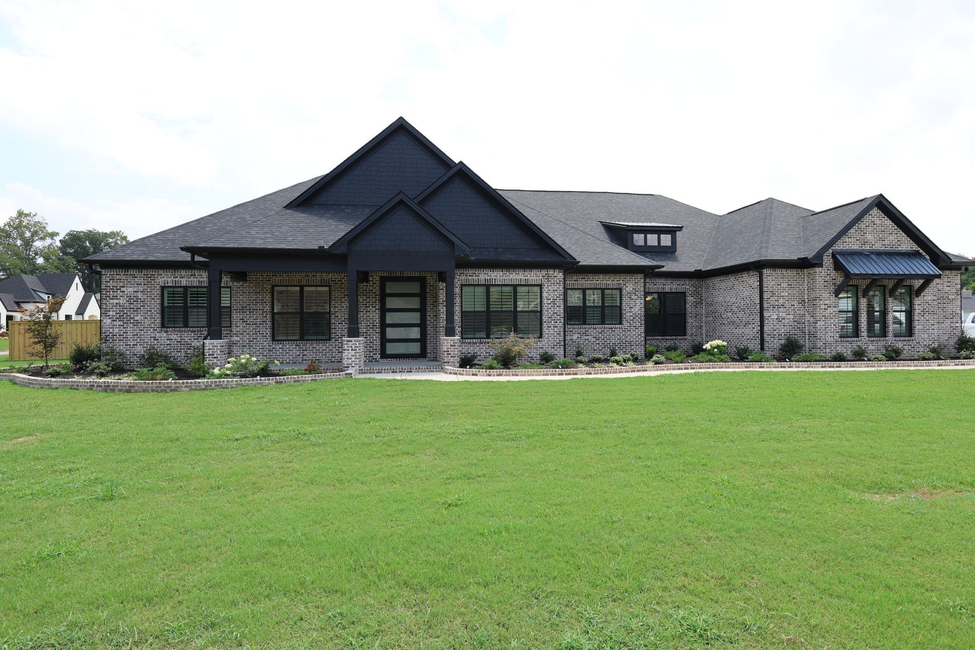 A one-story brick house with a dark roof and black trim sits on a green lawn.
