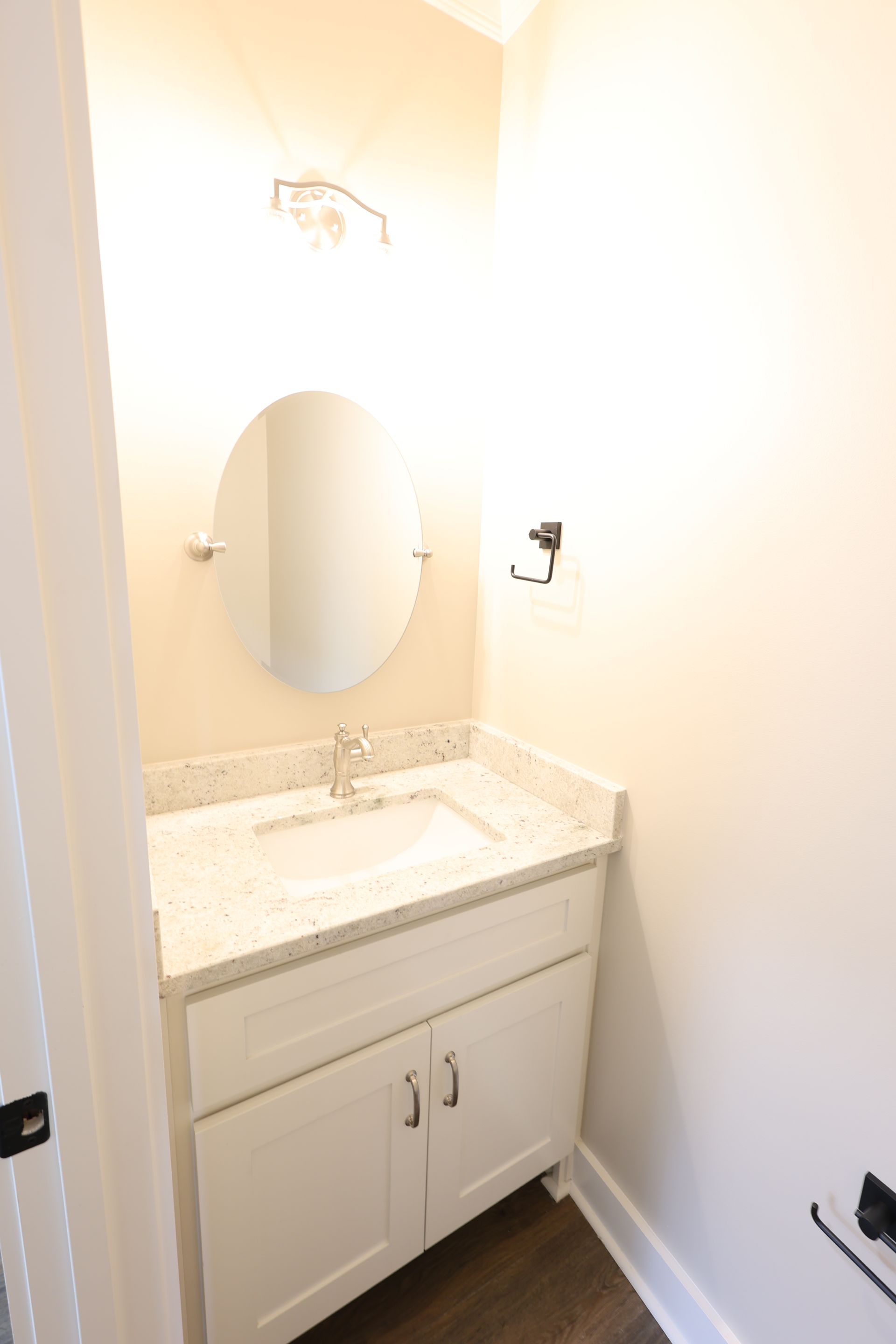 Small bathroom with white vanity, oval mirror, and light fixture.