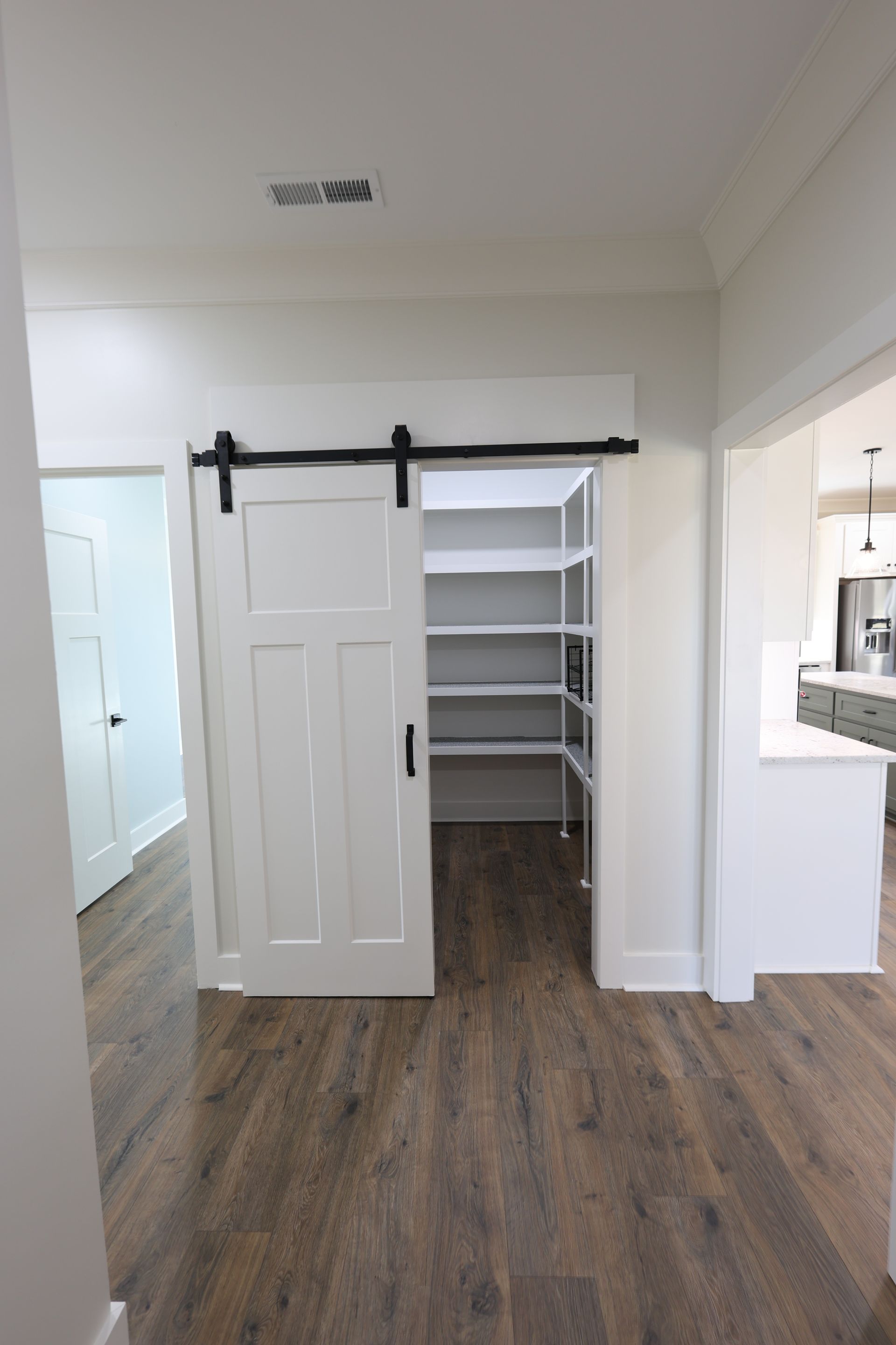 White pantry with barn door, shelves, and wood floors.