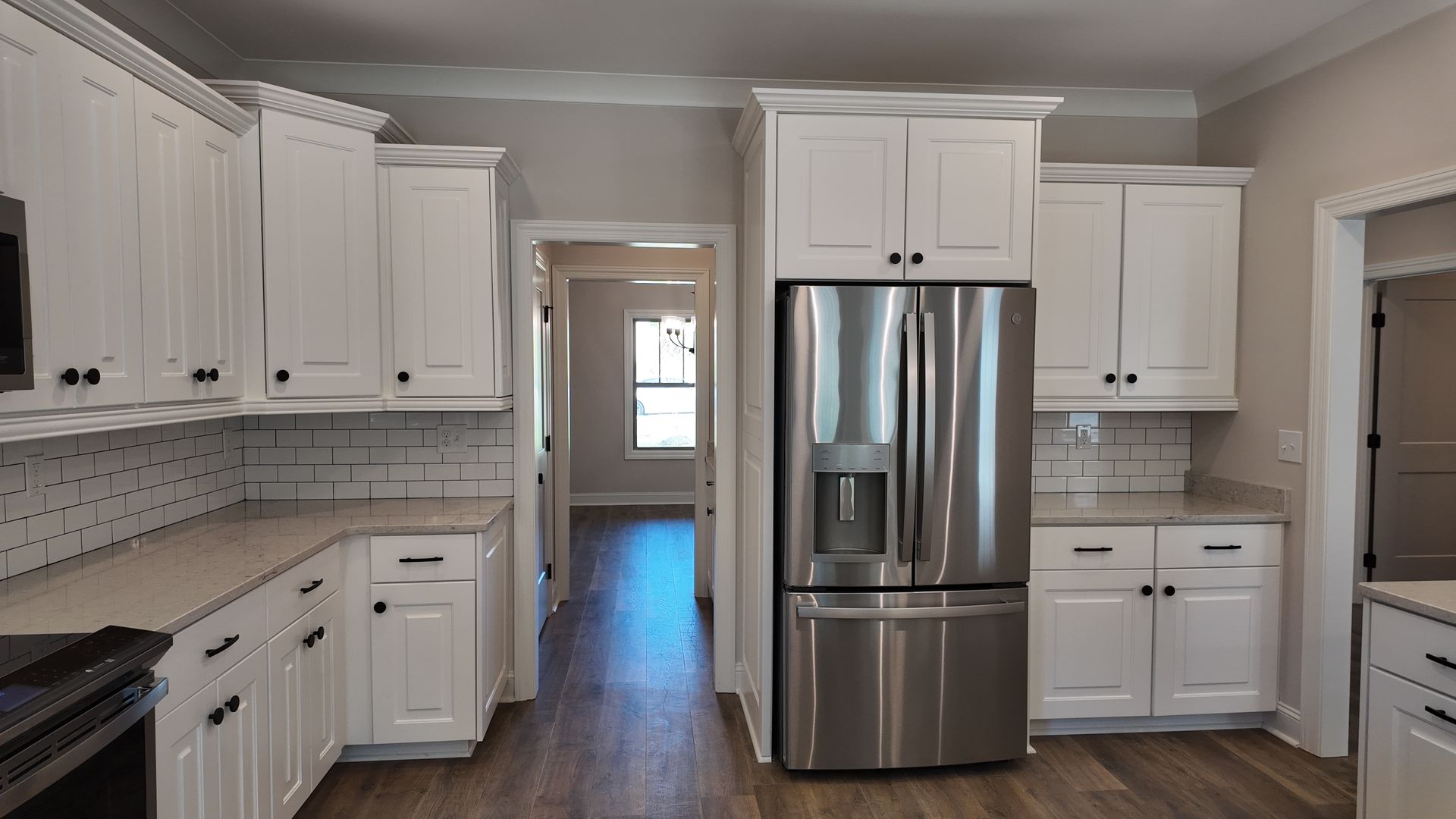 White kitchen with stainless steel refrigerator, cabinets, and light countertops.