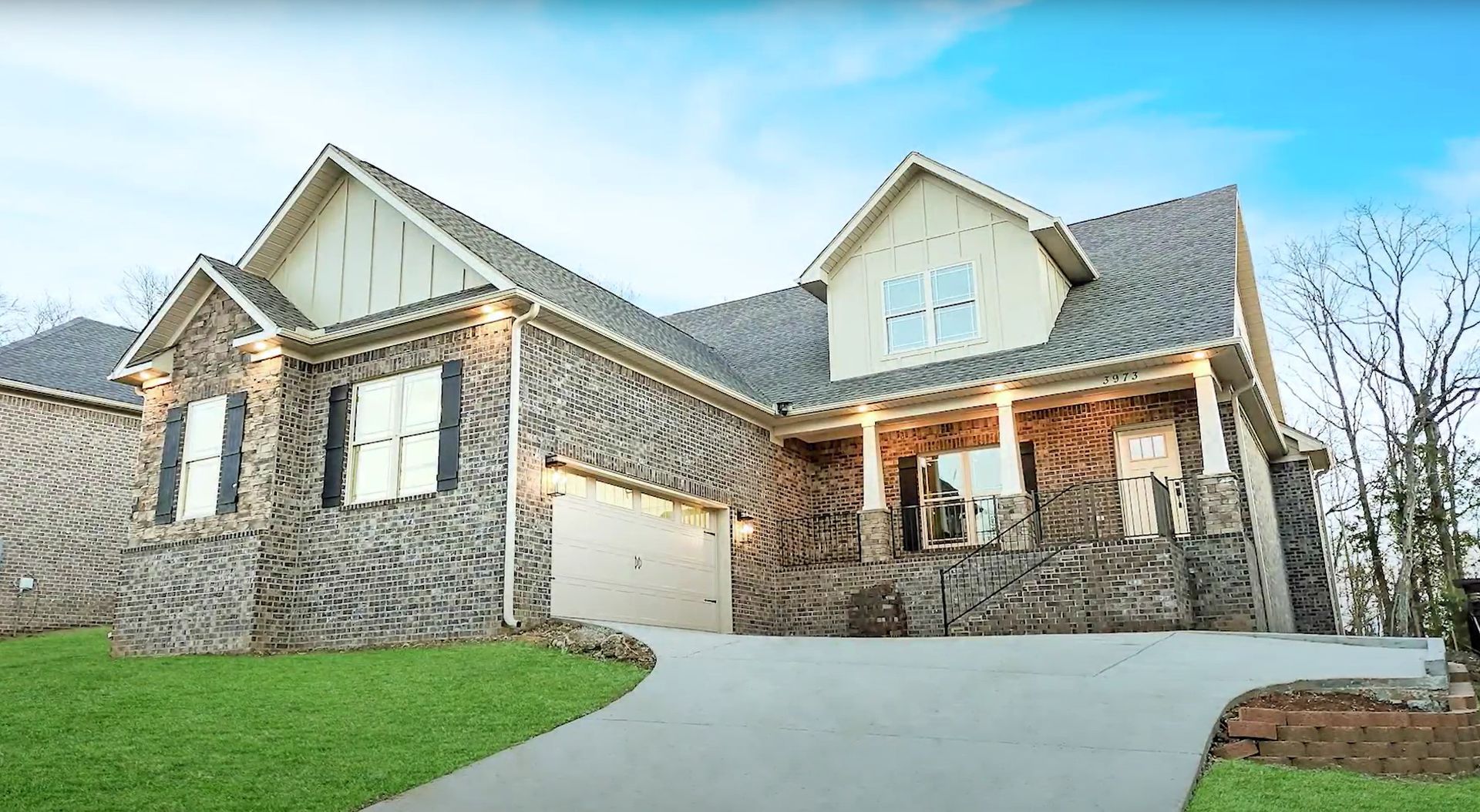 A two-story house with stone siding, a driveway, and green lawn under a blue sky.
