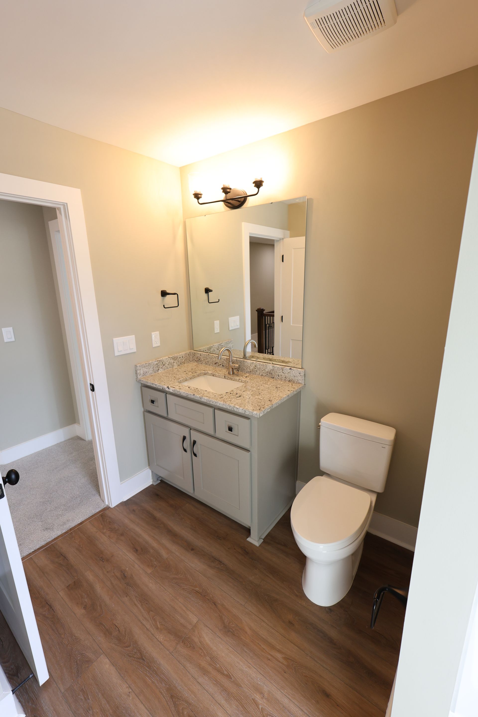 Bathroom with a gray vanity, granite countertop, toilet, and wooden floor.